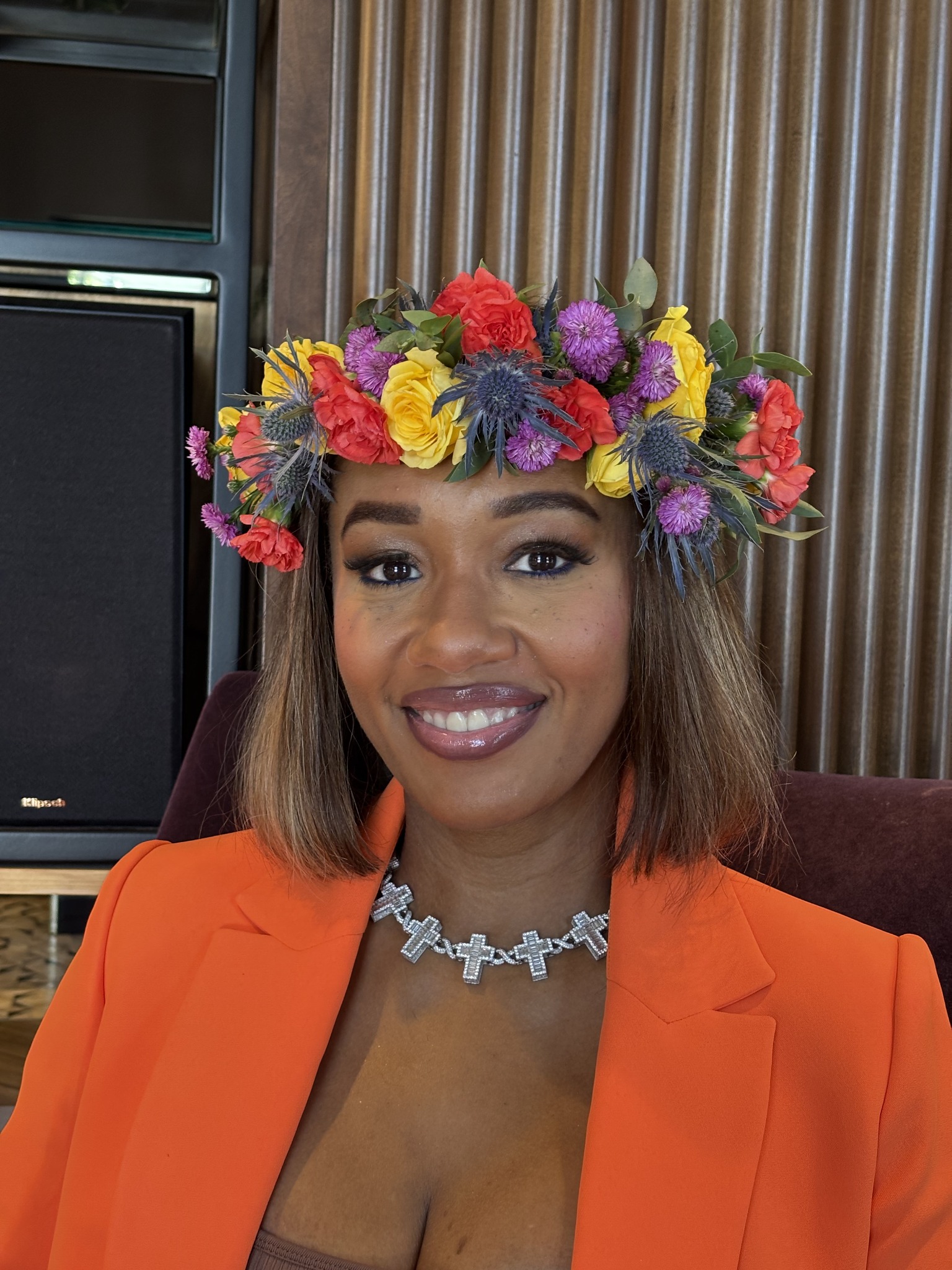 Alexis Jenee smiling in an orange blazer and colorful floral crown