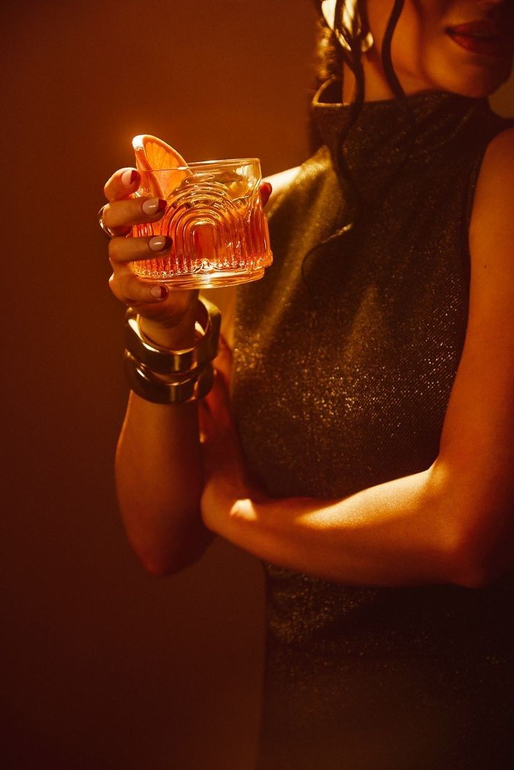 A woman holding an amber cocktail in warm golden light