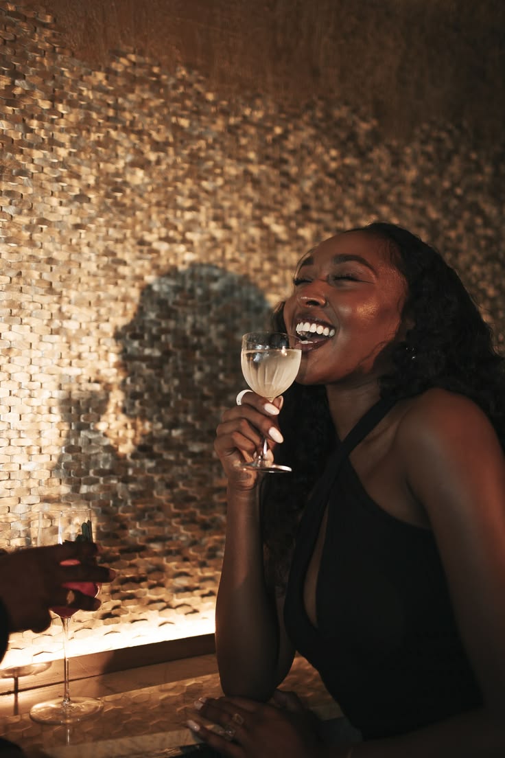 A Black woman laughing with a glass of wine in a warmly lit room