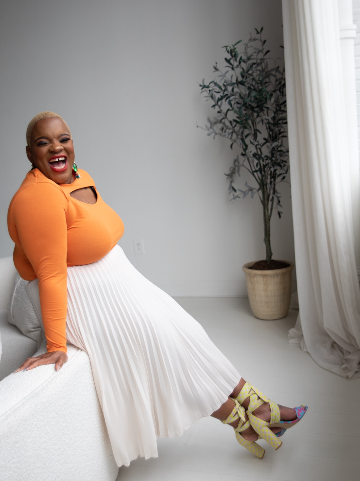 Ronisha laughing in an orange top and flowing cream skirt