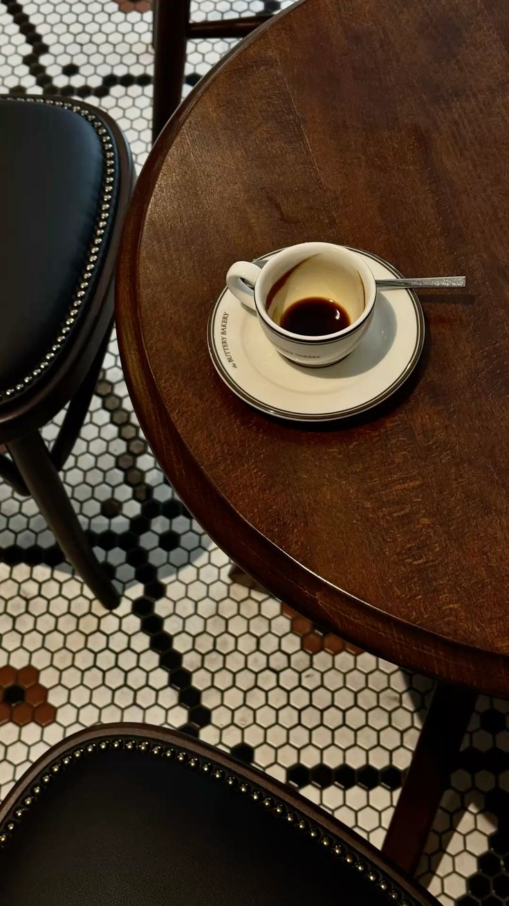 Espresso on a dark wood café table above a vintage penny tile floor