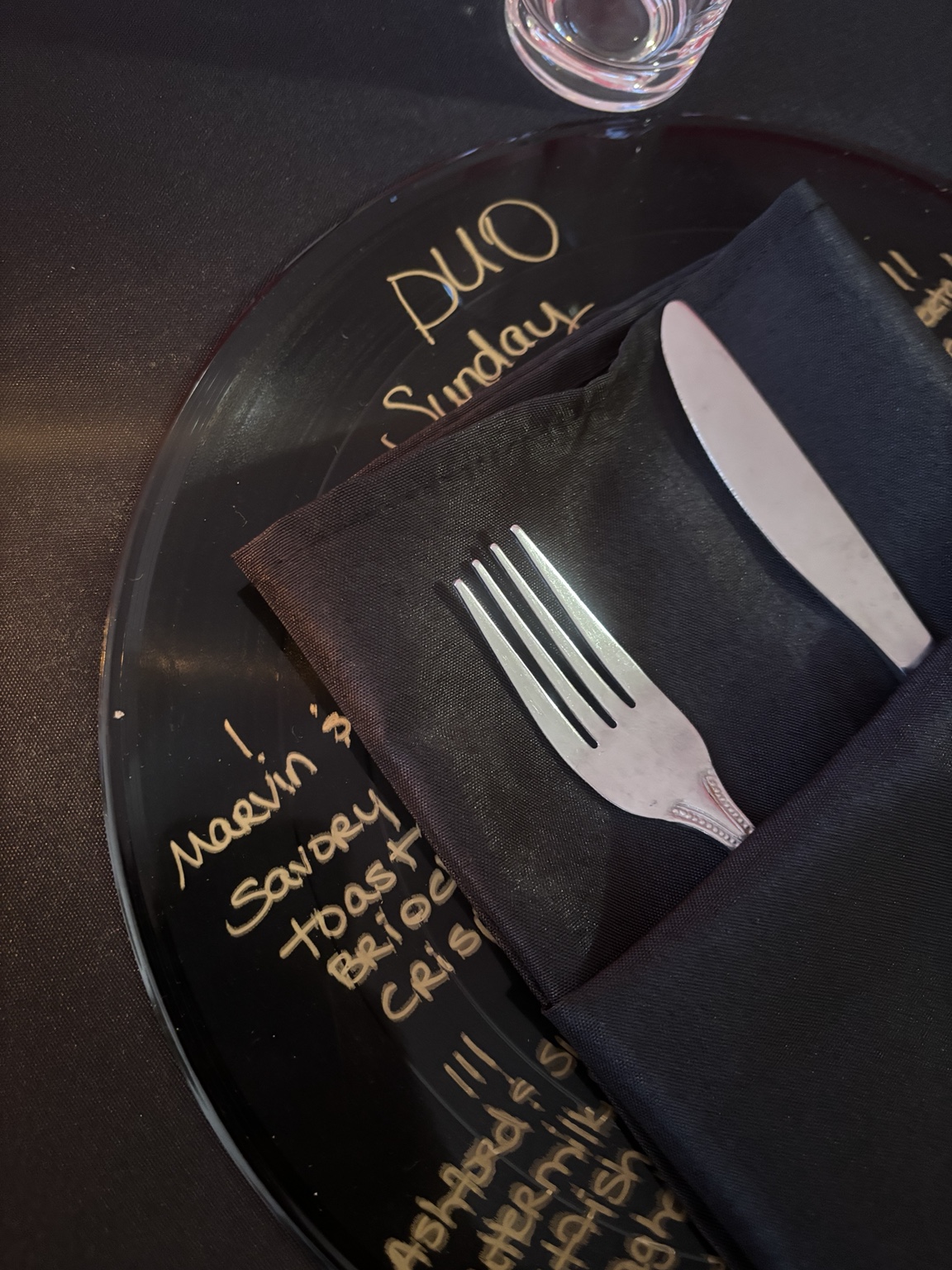 Close view of a handwritten gold DUO menu on a black vinyl record place setting